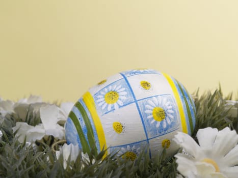 handpainted daisy design on easter egg, artificial grass and blossoms, yellow background