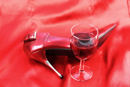 Red wine and shoe on red satin background