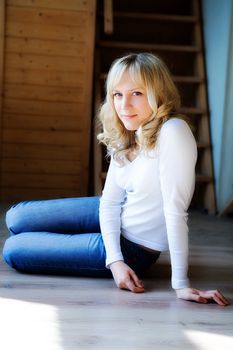 The fair-haired girl in jeans sits on a floor
