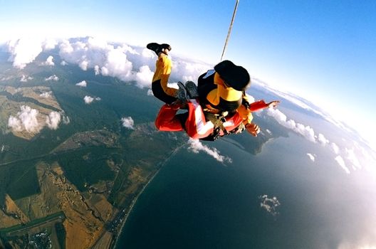 Aerial view of skydivers with parachute cord falling to earth over ocean.