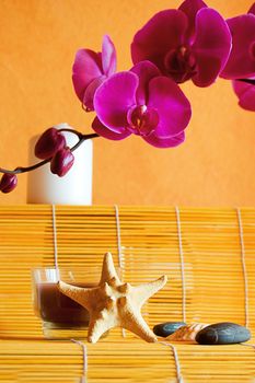 candles, orchids and stones on orange, spa concept