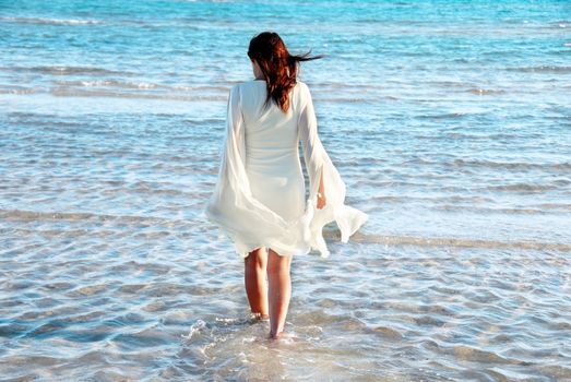 woman in white dress and raised hands walking in blue sea water