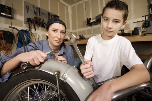 Hispanic mother and son working on motorcycle in garage