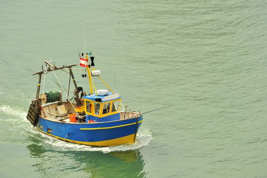 A small fishing boat coming into harbour. Space for text on the water.