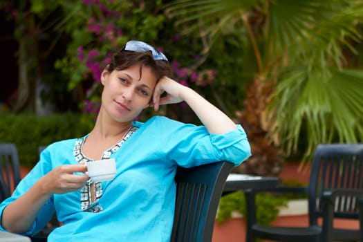 yong woman sitting on a chair in a garden  drinking coffee