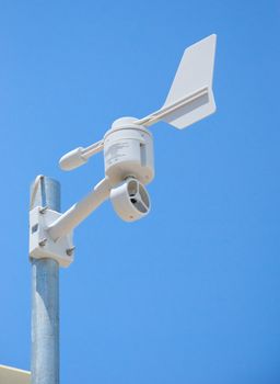 A white weather station mounted to a steel pole shot against a clear blue sky