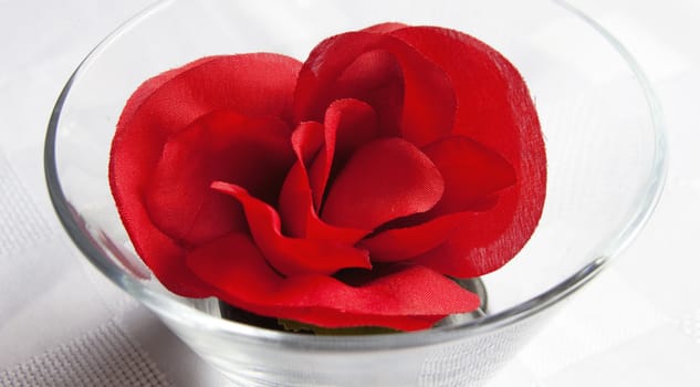 Red fabric rose sits nestled in a glass dish on white linen