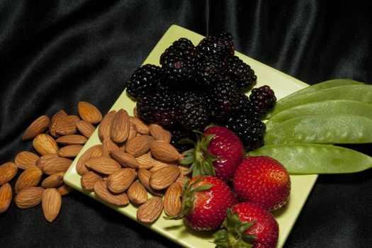 Berries, nuts, and snow pea pods on a light green plate against a black background are a healthy snack designed to refresh and keep fit