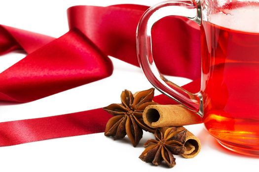 half glass with red tea, two cinnamon sticks, two star anise and a red ribbon on white background