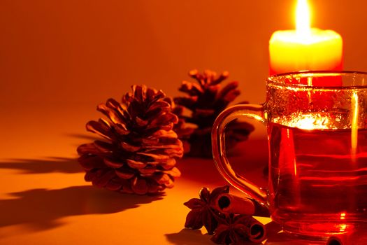 red tea in a glass, cinnamon sticks, star anise and a conifer cone at candle light