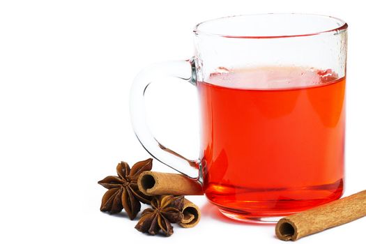 red tea in a glass, some cinnamon sticks and star anise on white background