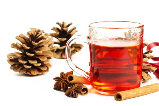 red tea in a glass, cinnamon sticks, star anise and some conifer cones on white background