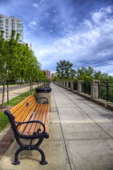 View of a bench along a sidewalk in a residential area near a river valley.