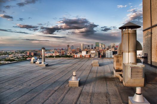 Vents on the roof of a skyscraper with the city in the background early in the evening.