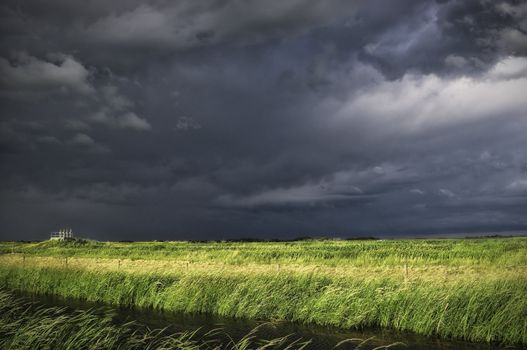 Water filled ditch and field with menacing dark clouds in the background.