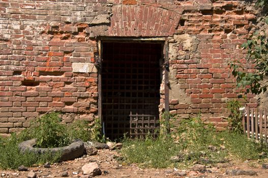 Old door with iron bars in a dilapidated brick wall.