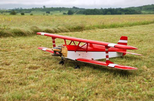 Red and white radio controlled aircraft with methanol engine on a grassy field.