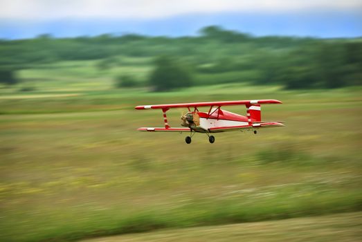 Red and white radio controlled aircraft with methanol engine flying over grassy field. The image shows motion blur.