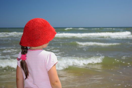 Girl in a red straw hat looking at the sea