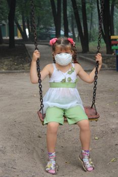 The girl in a breathing mask on a swing in a house court yard