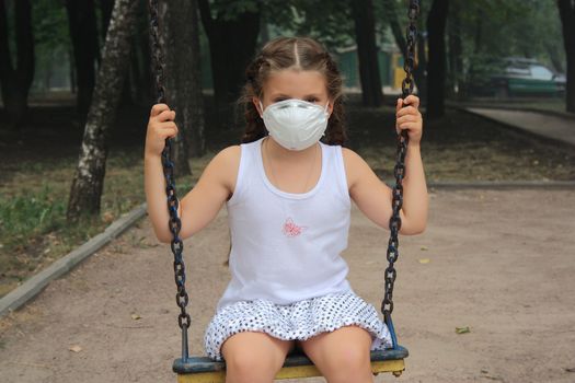 The girl in a breathing mask on a swing in a house court yard