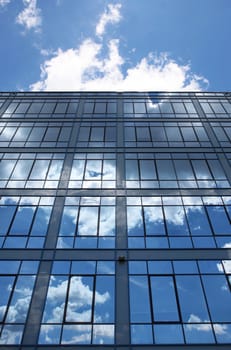 Modern glass building in perspective reflecting cloudy sky