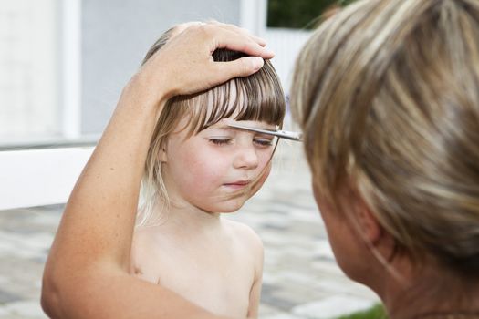 Woman cutting young girls hair outdoor
