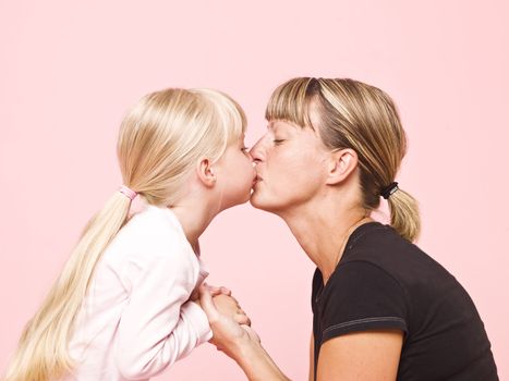 Mother and daughter kissing towards pink background