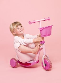 Young girl sitting on a scooter towards pink background