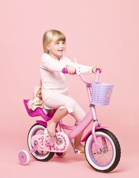 Young girl on her bike towards pink background