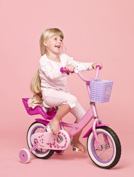 Young girl on her bike towards pink background