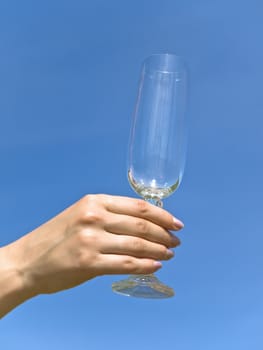 empty wineglass in woman hand against the blue sky