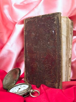 Old book with old clocks against the pink and red textile 