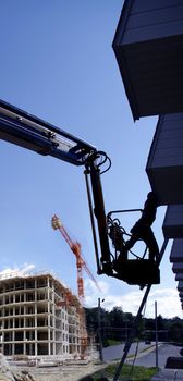 abstract dramatic composite of silhouette construction worker on a manlift elevator working with industrial building work in progress background .blue sky .