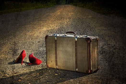 Old suitcase with red shoes left on a dirt road