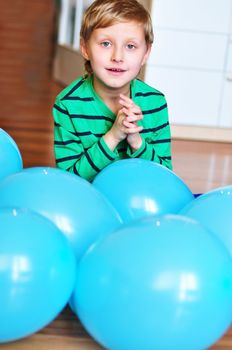 happy boy sitting with blue  balloons on the wooden floor
