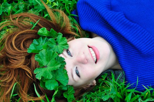 redheaded girl lating on the green grass with crown from leaves