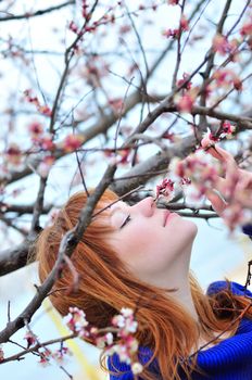 redheaded girl smelling blossom of peach tree