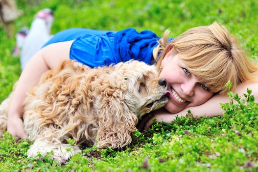 woman and dog laying on the meadow, dog lickig woman's cheek
