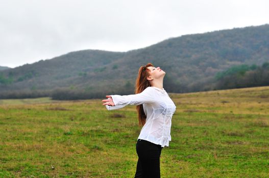 redheaded girl standing in fielad at one with nature, 	boughs reach out towards the sun