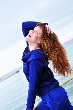 laughing redheaded girl wearing blue clothes near the sea 