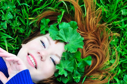 face of redheaded girl laying on the green grass with crown from leaves