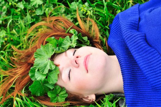 redheaded girl laying on the green grass with crown from leaves her eyes are closed
