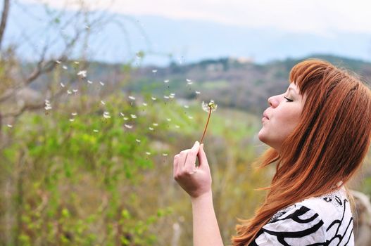 pretty redheaded teen girl blowing on dandelion
