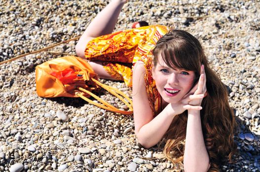 bright longhaired  girl in orange dress laying on the pebble