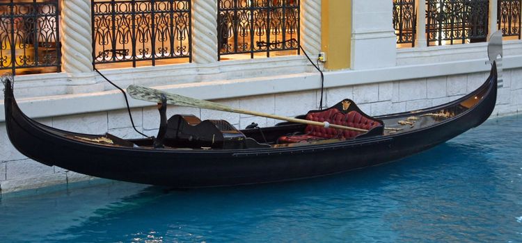 A gondola sitting in a canal of blue water.
