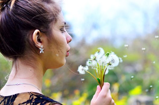 teen pretty girl blowing on many dandelions
