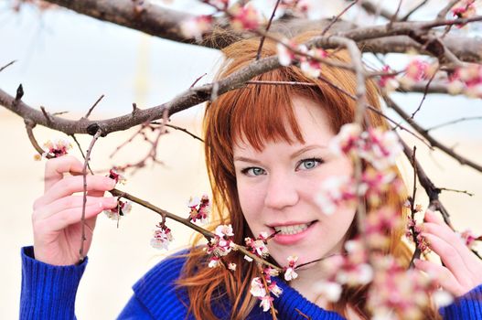 redheaded girl smelling blossom of peach tree

