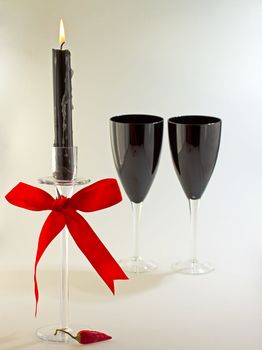 Black candle with red ribbon, two black glasses and a red chili pepper