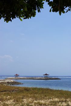 It's a view from the beach of Indian ocean with a blue sky and two little temple in Bali